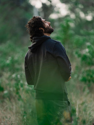 Man standing in a forest, looking up at the trees