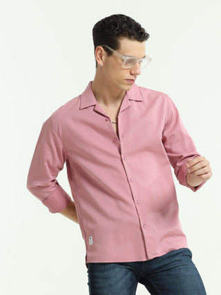 Man wearing a pink casual shirt and blue jeans, looking down while posing against a white studio background.