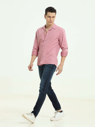 Man wearing a pink casual shirt, blue jeans, and white sneakers walking in a white studio background.