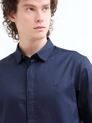 Close-up of a man wearing a navy blue casual shirt, looking to the side against a white studio background.