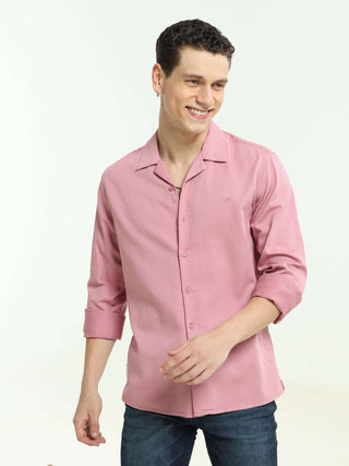 Man wearing a pink casual shirt and blue jeans, smiling while posing against a white studio background.