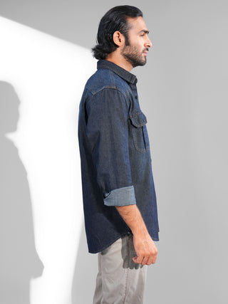 Man wearing a dark denim shirt and showing right side of the shirt against a plain background.