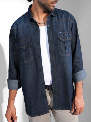 Man wearing a dark denim shirt over a white t-shirt on a plain background.