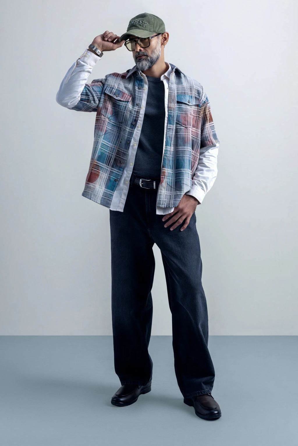 Man wearing a Oversize shirt, black pants, and a cap against a plain background.