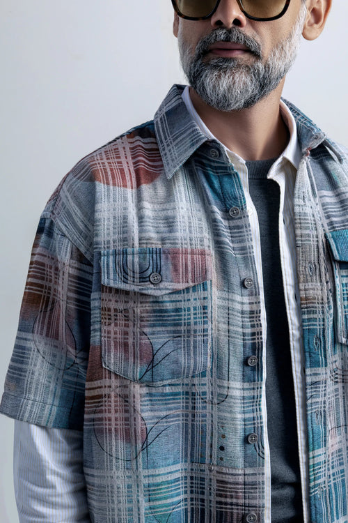  A close-up of a man with a beard wearing a loose plaid shirt, highlighting his expression and the shirt's design.