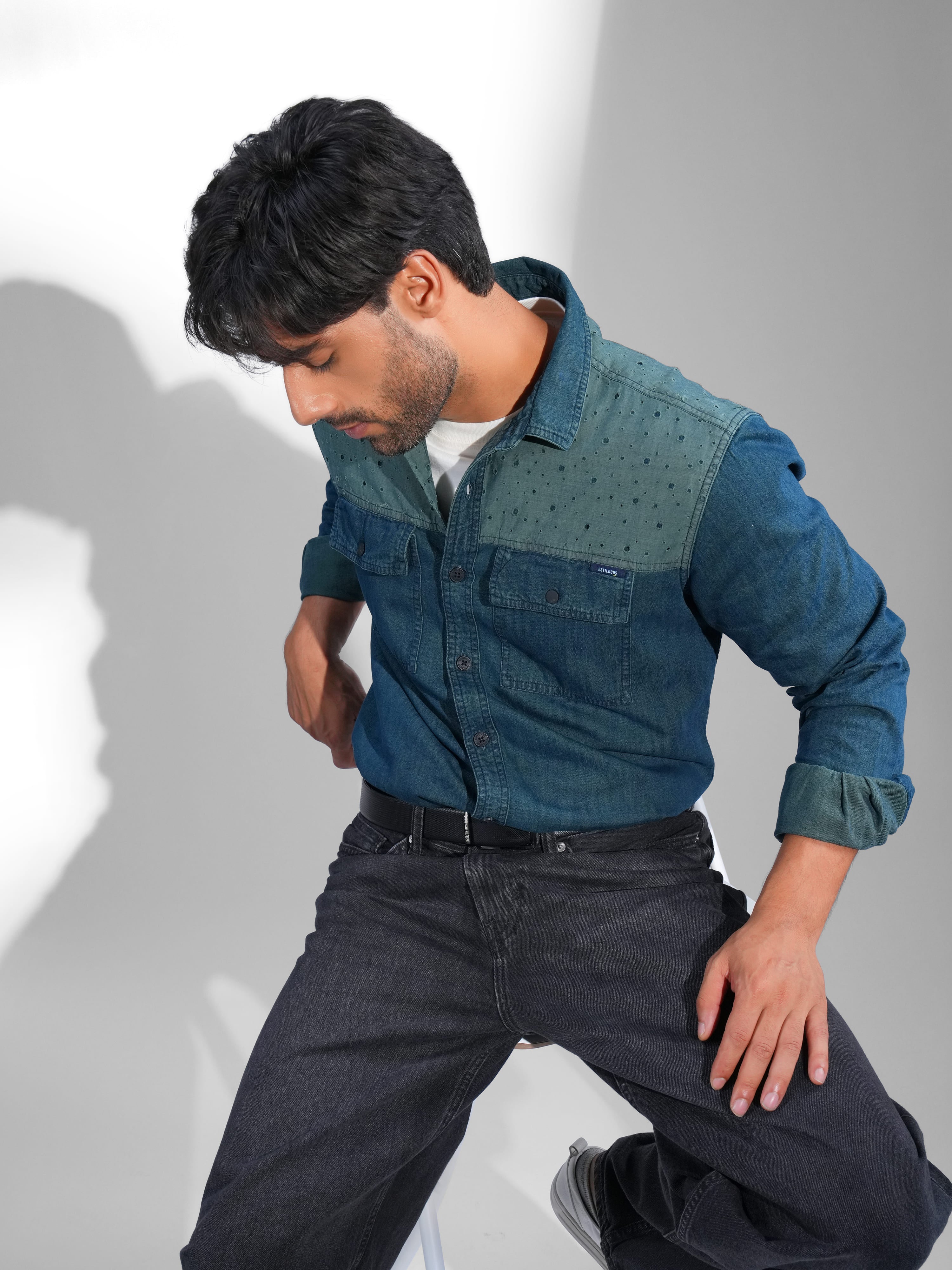 Man wearing a blue denim shirt and dark jeans against a white background