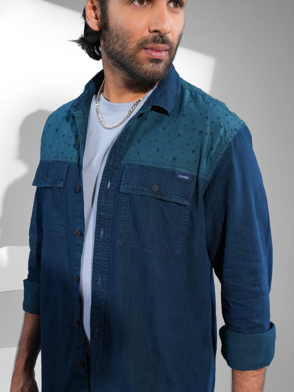 Man wearing a blue denim shirt over a white t-shirt against a white background.