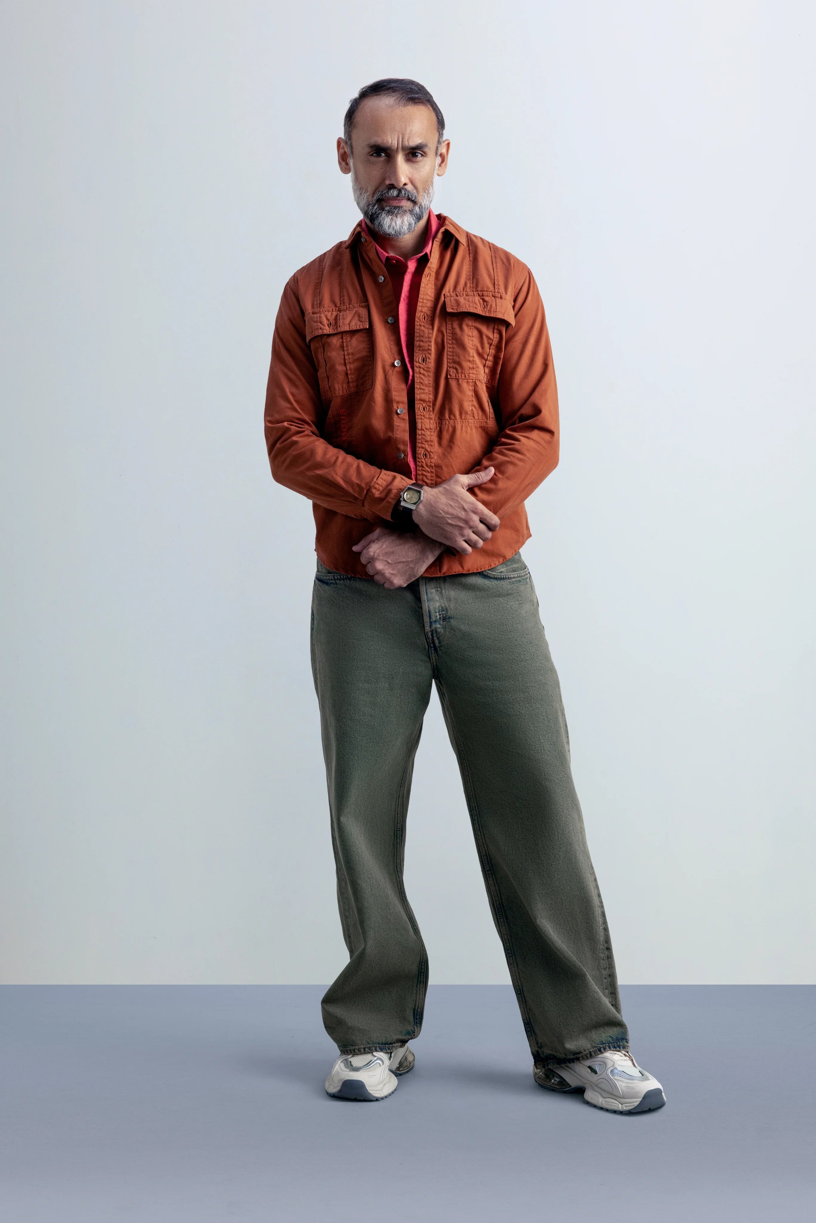 Man wearing an jacket and green pants standing against a plain background.