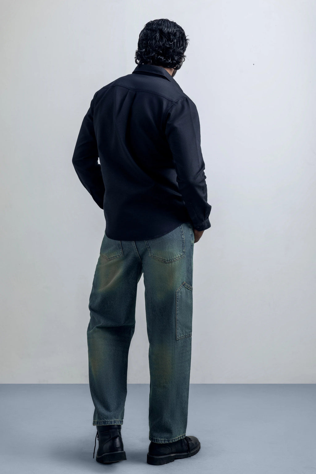Person wearing a shirt and blue jeans standing against a plain background.