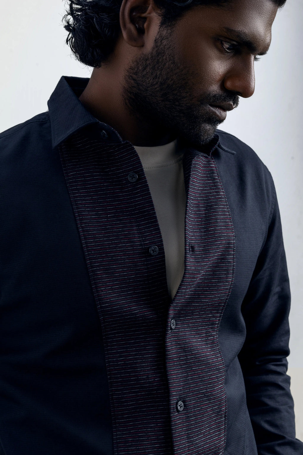 Man wearing a dark blue shirt with a patterned design on a plain background.