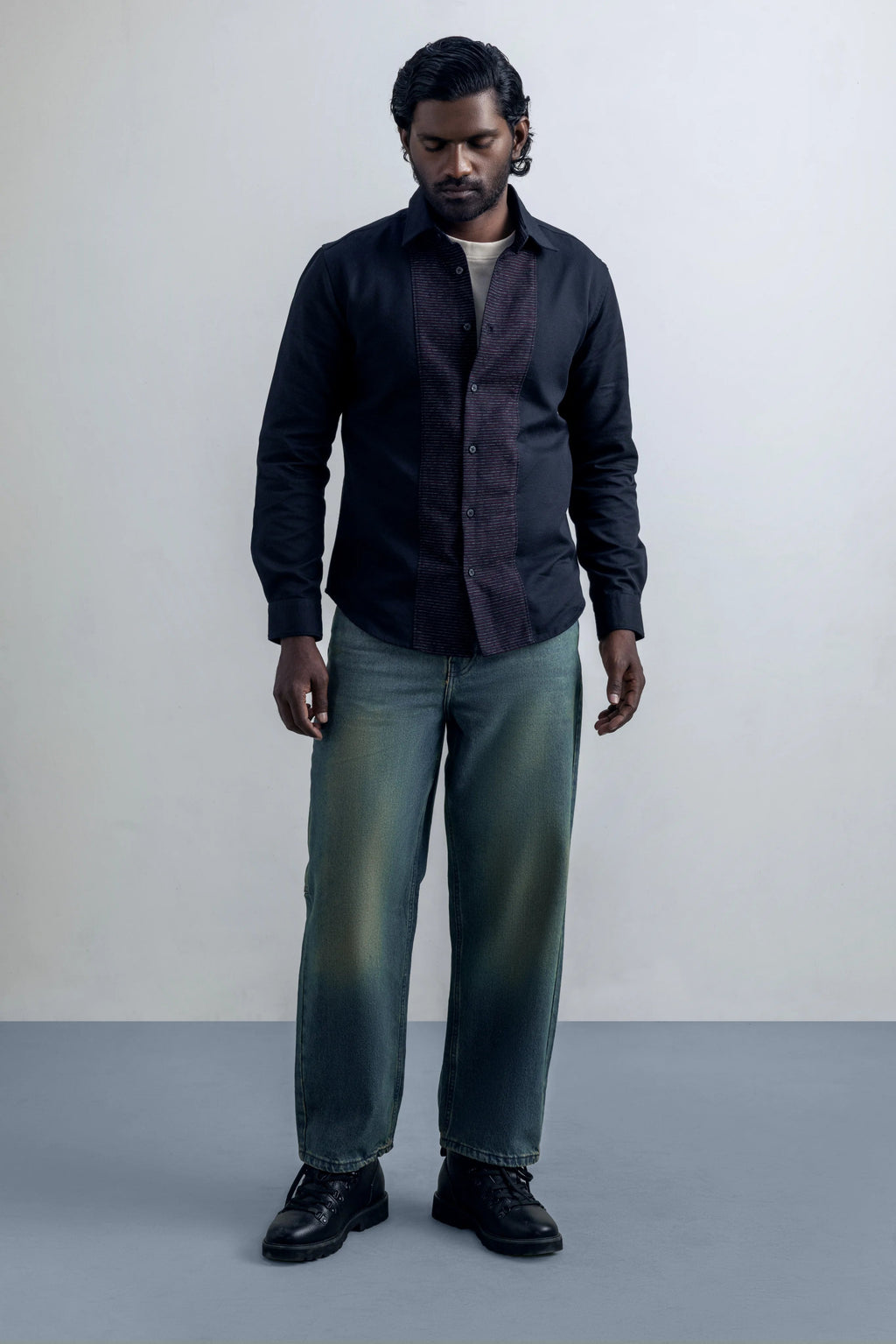 Man wearing a dark shirt, light pants, and black shoes against a plain background.