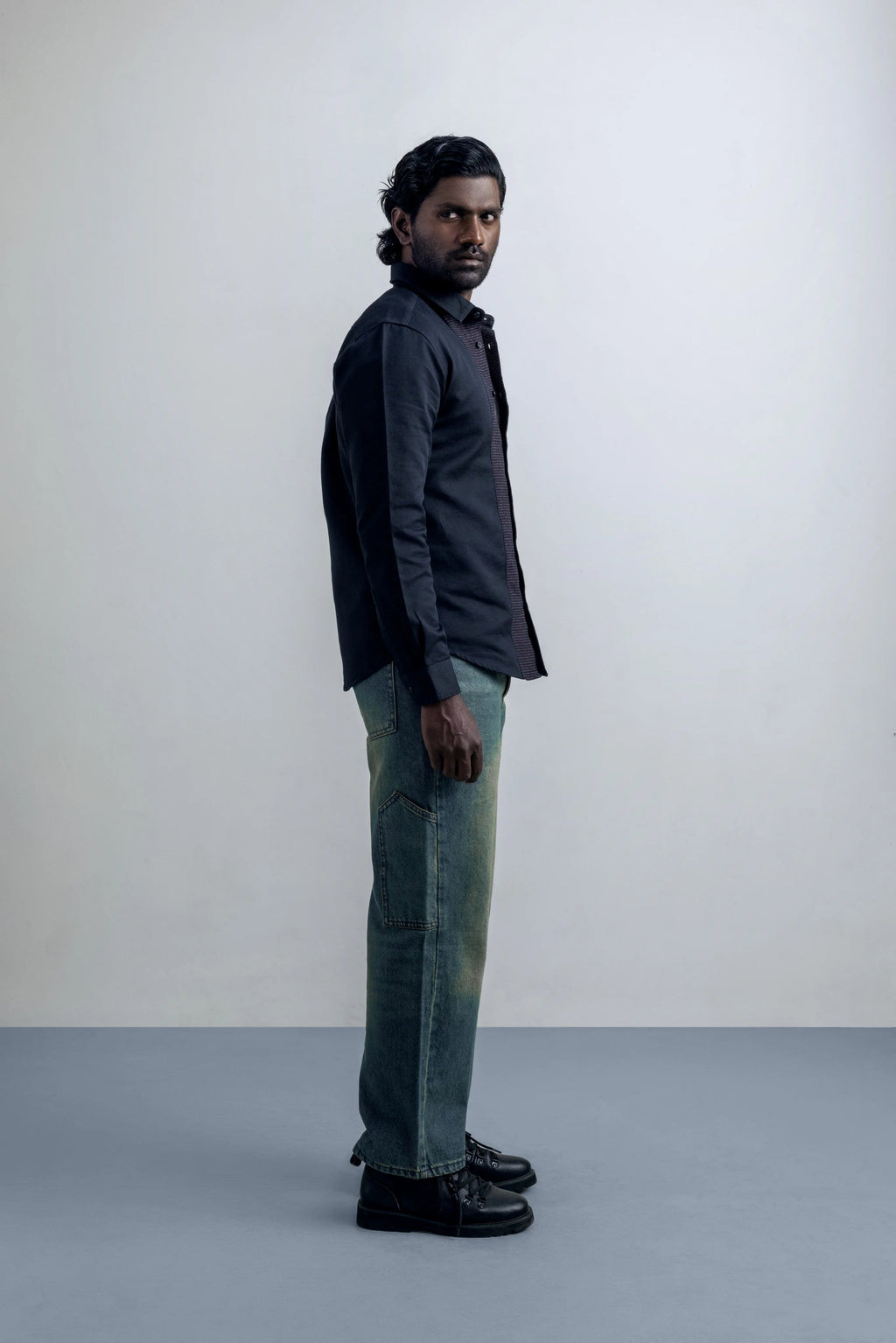 Man wearing a dark shirt and light jeans standing against a plain background