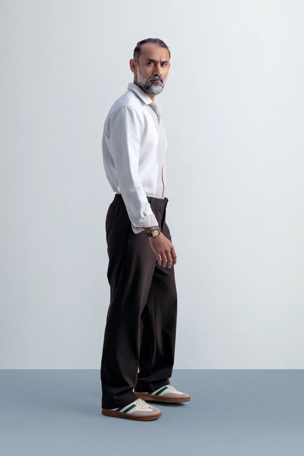 Man wearing a white shirt and dark pants against a plain background
