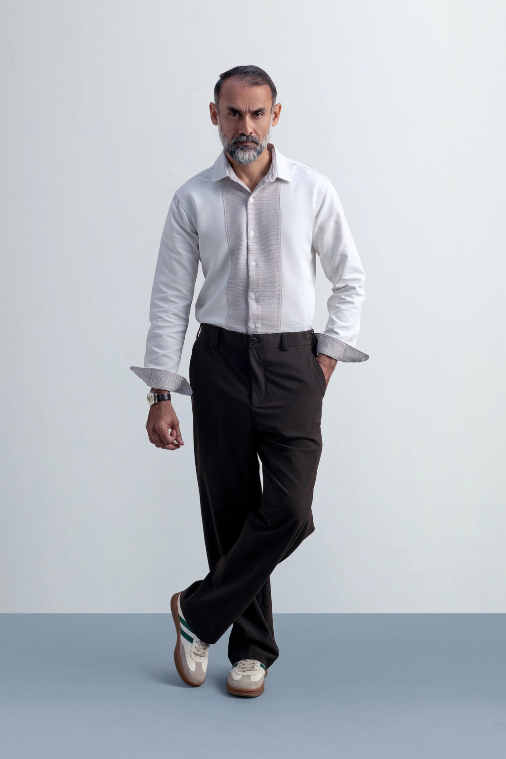 Man wearing a white shirt and dark pants against a white background.