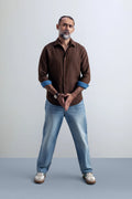 Man wearing a brown shirt and blue jeans against a white background.