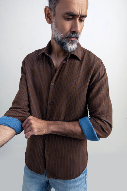 Man wearing a brown shirt with rolled-up sleeves against a white background.