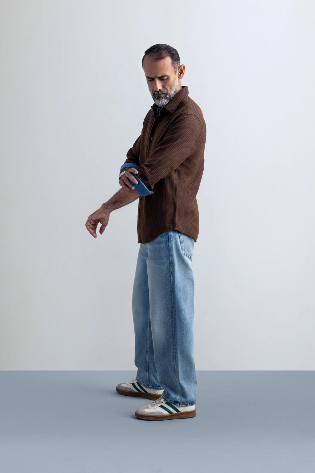 Man wearing a brown shirt and blue jeans against a plain background.