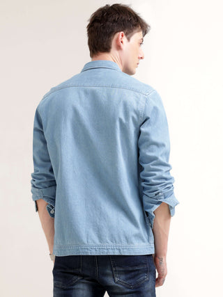Person wearing a light blue denim jacket on a plain background