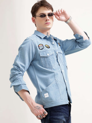 Man wearing a light blue denim jacket with patches on a white background.