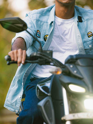 Person wearing a denim jacket with patches on a motorcycle