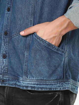 Hand reaching into a pocket of a blue denim jacket.