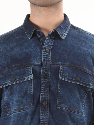 Close-up of a person wearing a blue denim shirt with a white background.