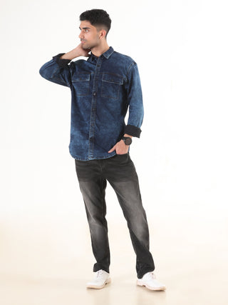 Man wearing a blue denim shirt and black jeans on a white background.