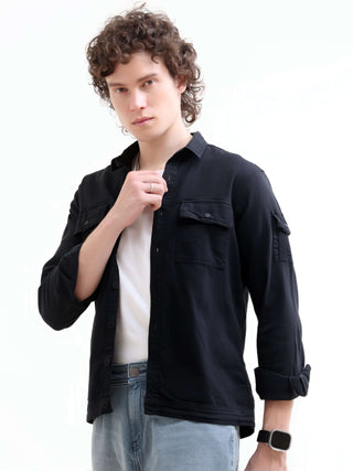 Man wearing a black denim shirt  over a white T shirt and Standing against white background. 