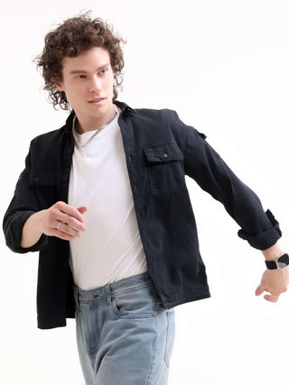 Man wearing a black jacket over a white shirt and blue jeans on a white background.