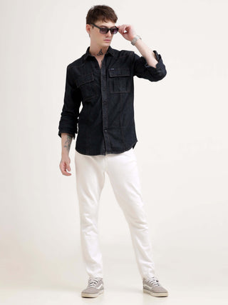 Person wearing a black denim shirt and white pants on a white background.