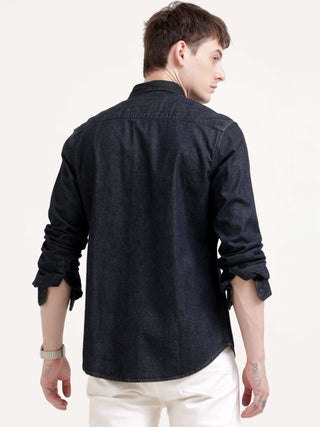 Man showing backside of his shirt  wearing a black denim shirt on a white background.